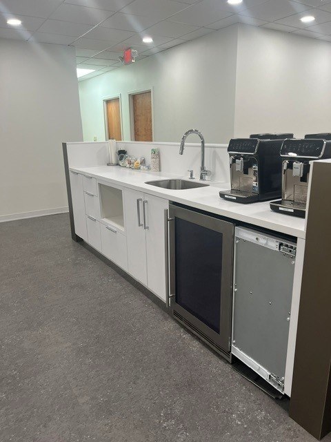 The coffee station with two espresso machines, a sink and a beverage fridge